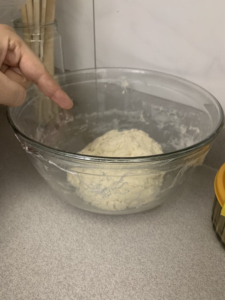 Bowl with dough and plastic wrap on top.