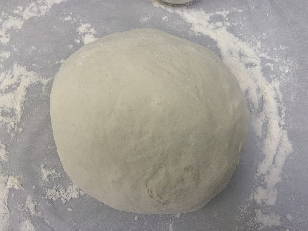 A reshaped doughball resting on a piece of parchment paper.