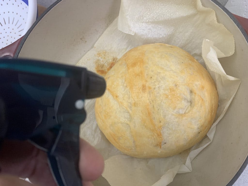 A gently cooked loaf of bread that's been taken out with a spray bottle of water next to it.